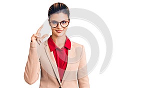 Young beautiful woman wearing business shirt and glasses smiling and confident gesturing with hand doing small size sign with