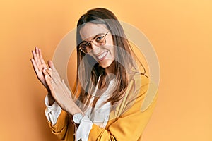 Young beautiful woman wearing business style and glasses clapping and applauding happy and joyful, smiling proud hands together