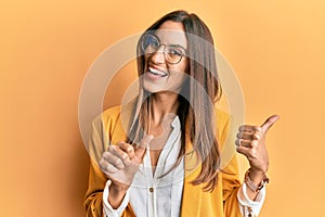 Young beautiful woman wearing business style and glasses pointing to the back behind with hand and thumbs up, smiling confident