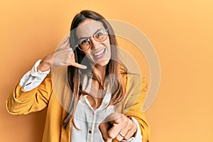 Young beautiful woman wearing business style and glasses smiling doing talking on the telephone gesture and pointing to you