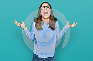Young beautiful woman wearing casual clothes and glasses crazy and mad shouting and yelling with aggressive expression and arms