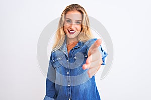 Young beautiful woman wearing casual denim shirt standing over isolated white background smiling friendly offering handshake as