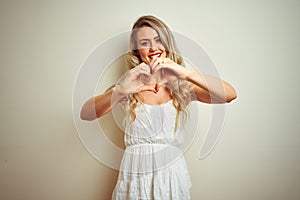 Young beautiful woman wearing casual dress standing over white  background smiling in love showing heart symbol and shape