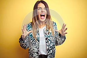 Young beautiful woman wearing casual jacket over yellow isolated background crazy and mad shouting and yelling with aggressive