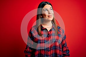 Young beautiful woman wearing casual shirt over red background smiling looking to the side and staring away thinking