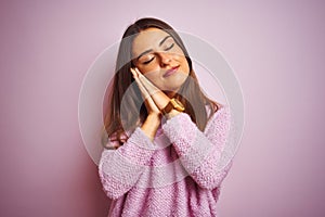 Young beautiful woman wearing casual sweater standing over isolated pink background sleeping tired dreaming and posing with hands