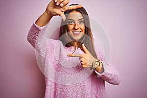 Young beautiful woman wearing casual sweater standing over isolated pink background smiling making frame with hands and fingers