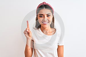 Young beautiful woman wearing casual t-shirt and diadem over isolated white background showing and pointing up with finger number