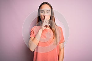 Young beautiful woman wearing casual t-shirt standing over isolated pink background asking to be quiet with finger on lips