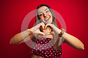 Young beautiful woman wearing casual t-shirt standing over isolated red background smiling in love showing heart symbol and shape