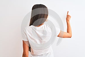 Young beautiful woman wearing casual t-shirt standing over isolated white background Posing backwards pointing ahead with finger
