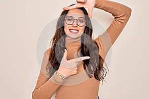 Young beautiful woman wearing casual turtleneck sweater and glasses over white background smiling making frame with hands and