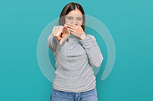 Young beautiful woman wearing casual turtleneck sweater laughing at you, pointing finger to the camera with hand over mouth, shame