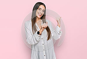 Young beautiful woman wearing casual white shirt pointing to the back behind with hand and thumbs up, smiling confident