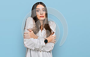 Young beautiful woman wearing casual white shirt shaking and freezing for winter cold with sad and shock expression on face