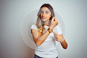 Young beautiful woman wearing casual white t-shirt over isolated background In hurry pointing to watch time, impatience, looking