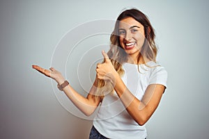 Young beautiful woman wearing casual white t-shirt over isolated background Showing palm hand and doing ok gesture with thumbs up,