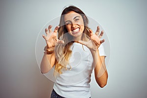 Young beautiful woman wearing casual white t-shirt over isolated background smiling funny doing claw gesture as cat, aggressive