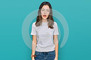 Young beautiful woman wearing casual white t shirt in shock face, looking skeptical and sarcastic, surprised with open mouth