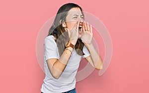 Young beautiful woman wearing casual white t shirt shouting angry out loud with hands over mouth