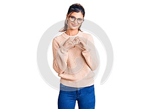 Young beautiful woman wearing casual winter sweater and glasses smiling in love showing heart symbol and shape with hands