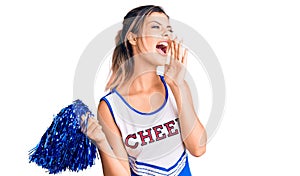 Young beautiful woman wearing cheerleader uniform shouting and screaming loud to side with hand on mouth