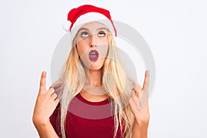 Young beautiful woman wearing Christmas Santa hat over isolated white background amazed and surprised looking up and pointing with