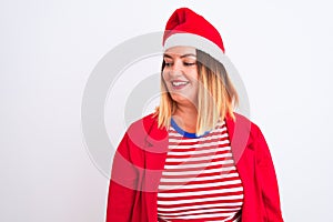 Young beautiful woman wearing Christmas Santa hat over isolated white background looking away to side with smile on face, natural