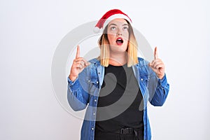 Young beautiful woman wearing Christmas Santa hat standing over isolated white background amazed and surprised looking up and