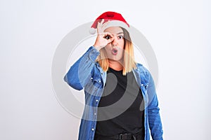 Young beautiful woman wearing Christmas Santa hat standing over isolated white background doing ok gesture shocked with surprised