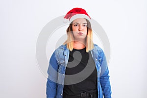 Young beautiful woman wearing Christmas Santa hat standing over isolated white background puffing cheeks with funny face