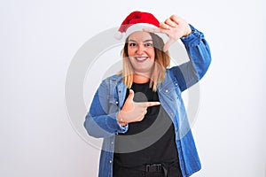 Young beautiful woman wearing Christmas Santa hat standing over isolated white background smiling making frame with hands and