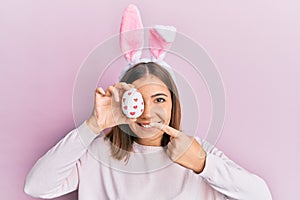 Young beautiful woman wearing cute easter bunny ears holding egg smiling happy pointing with hand and finger