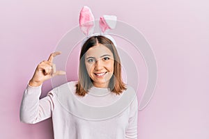 Young beautiful woman wearing cute easter bunny ears smiling and confident gesturing with hand doing small size sign with fingers