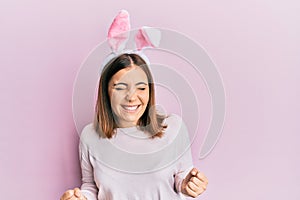Young beautiful woman wearing cute easter bunny ears very happy and excited doing winner gesture with arms raised, smiling and
