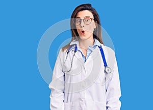 Young beautiful woman wearing doctor stethoscope and glasses afraid and shocked with surprise expression, fear and excited face