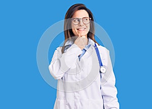 Young beautiful woman wearing doctor stethoscope and glasses with hand on chin thinking about question, pensive expression