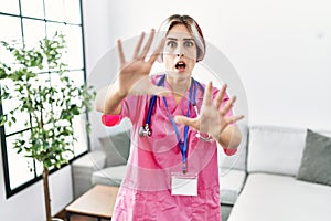 Young beautiful woman wearing doctor uniform and stethoscope afraid and terrified with fear expression stop gesture with hands,