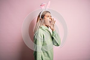 Young beautiful woman wearing easter rabbit ears standing over isolated pink background shouting and screaming loud to side with