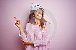 Young beautiful woman wearing funny cat cap standing over pink isolated background with a big smile on face, pointing with hand