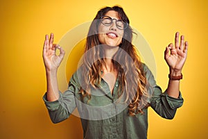 Young beautiful woman wearing green shirt and glasses over yelllow isolated background relax and smiling with eyes closed doing