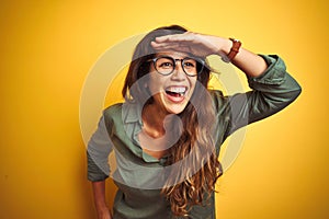 Young beautiful woman wearing green shirt and glasses over yelllow isolated background very happy and smiling looking far away