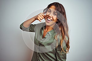 Young beautiful woman wearing green shirt standing over grey isolated background smiling doing phone gesture with hand and fingers