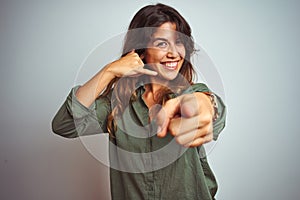 Young beautiful woman wearing green shirt standing over grey isolated background smiling doing talking on the telephone gesture