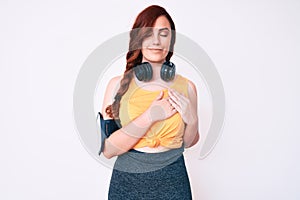 Young beautiful woman wearing gym clothes and using headphones smiling with hands on chest with closed eyes and grateful gesture