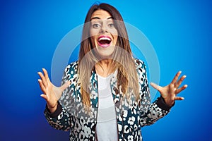 Young beautiful woman wearing a jacket standing over blue isolated background crazy and mad shouting and yelling with aggressive