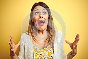 Young beautiful woman wearing jacket standing over yellow isolated background crazy and mad shouting and yelling with aggressive