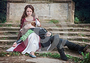 Young beautiful woman wearing medieval style dress with dagger holding friend on her knees with dagger on his neck