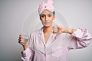 Young beautiful woman wearing pajama and sleep mask drinking glass of water with angry face, negative sign showing dislike with