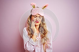 Young beautiful woman wearing pajama and sleep mask over pink isolated background touching mouth with hand with painful expression